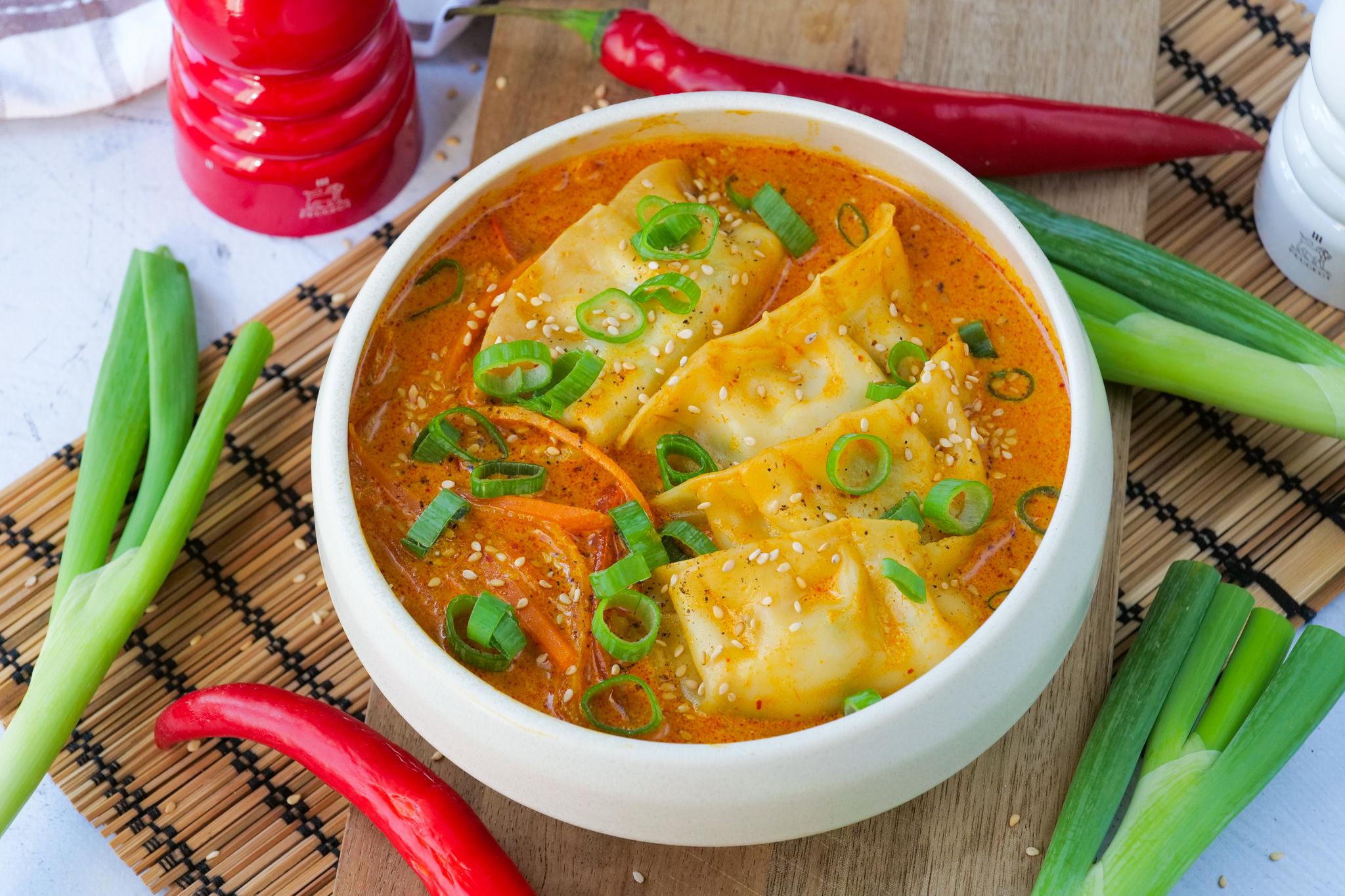 Bowl of coconut curry gyoza soup with julienned carrot and red bell pepper